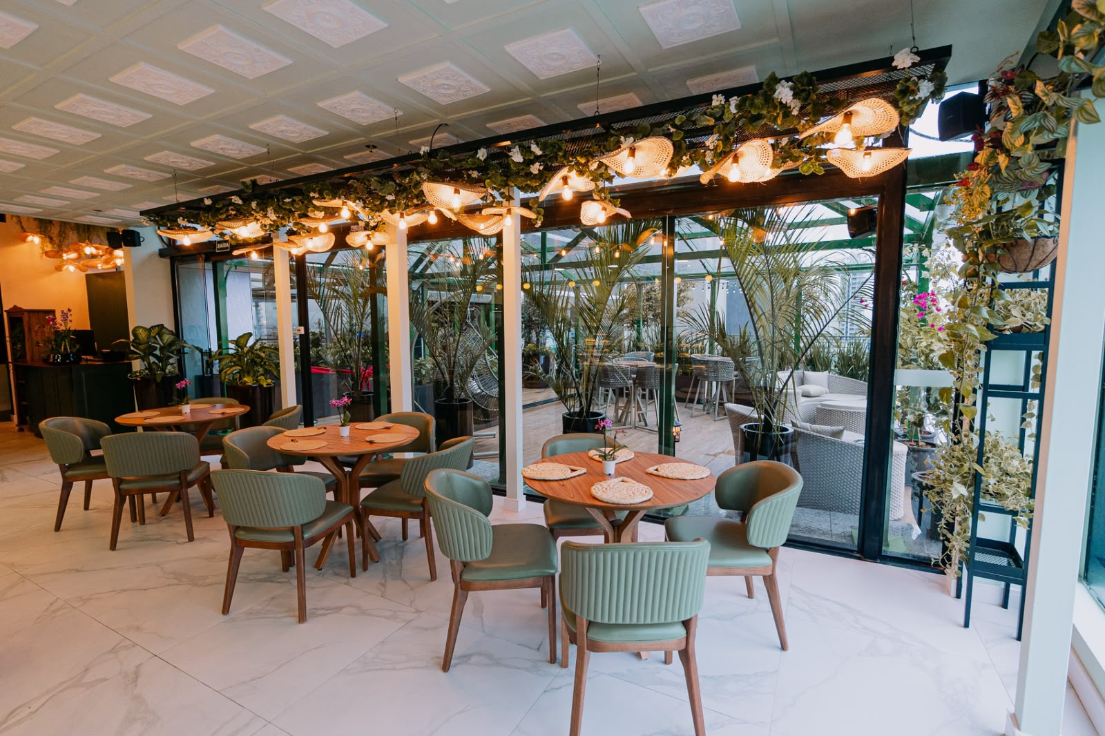 Ambiente com cadeiras verdes, plantas e iluminação decorativa